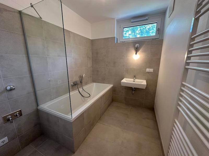 Modernes Badezimmer mit Badewanne, Duschwand aus Glas, Waschbecken und beheiztem Handtuchhalter.