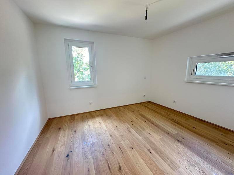 Helles Schlafzimmer mit zwei Fenstern, Holzboden und weißen Wänden, bereit zur Einrichtung.