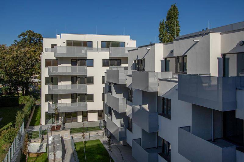 Moderne Wohngebäude mit mehreren Balkonen und einem gepflegten grünen Innenhof unter blauem Himmel.