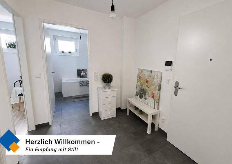 Heller Eingangsbereich mit dunklen Fliesen, weißer Kommode und Zugang zum Badezimmer.