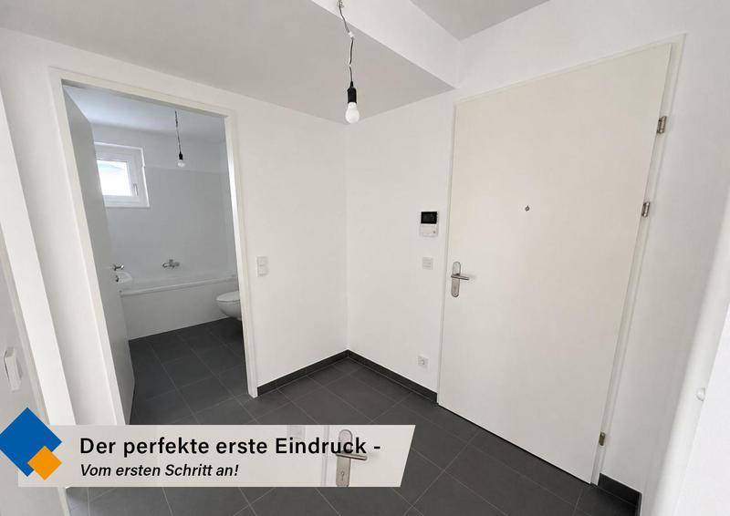 Heller Eingangsbereich mit dunklen Fliesen und offenem Zugang zu einem Badezimmer.