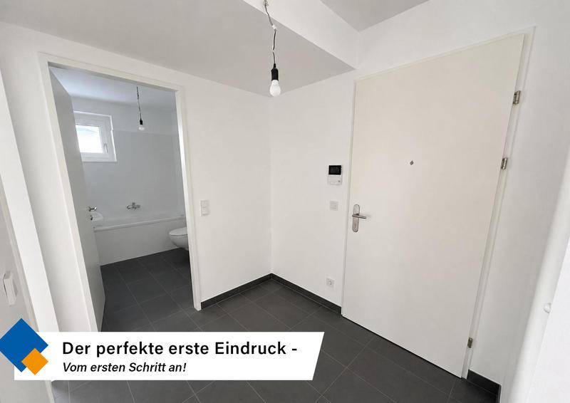 Heller Eingangsbereich mit dunklen Fliesen und Zugang zu einem Badezimmer.