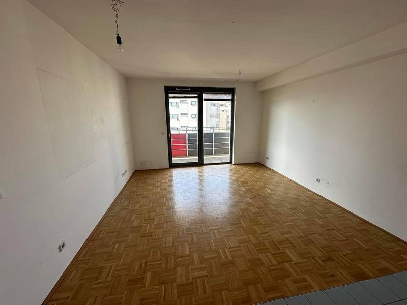 Geräumiges Wohnzimmer mit klassischem Parkettboden und großen Fenstern zum Balkon.
