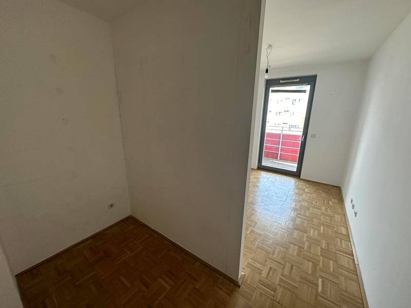 Schlafzimmer mit Parkettboden und Balkonzugang, teilweise durch eine Wand getrennt.