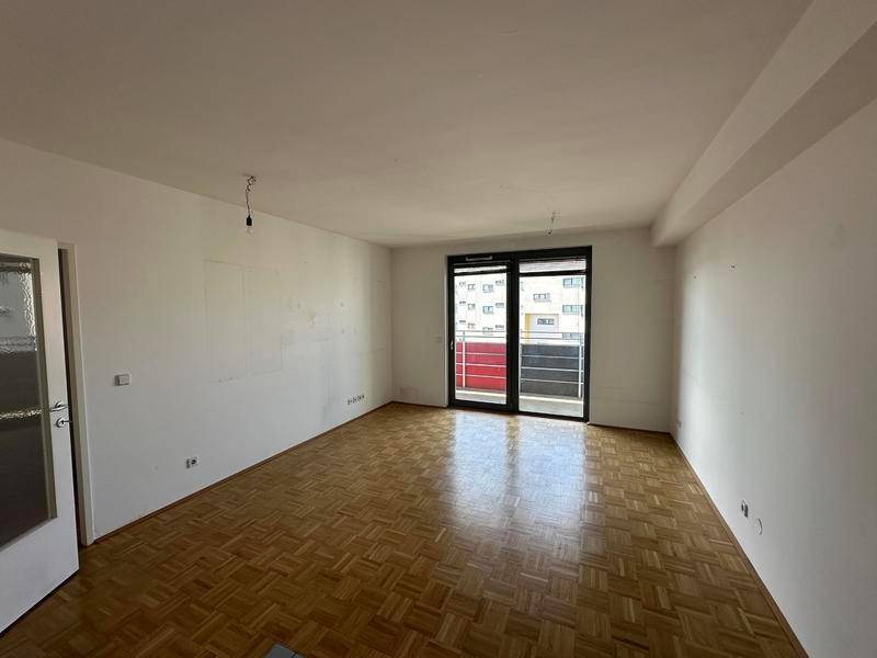 Helles Wohnzimmer mit Fischgrätparkettboden und Zugang zu einem Balkon.