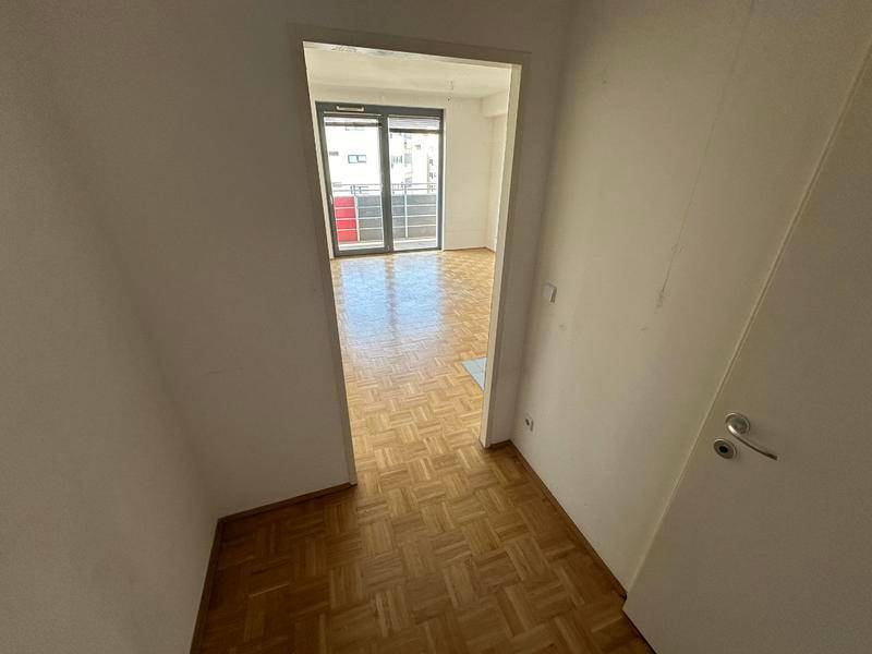 Heller Flur mit Parkettboden, der zu einem Wohnbereich mit Balkonzugang führt.