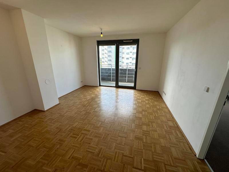 Helles Wohnzimmer mit Parkettboden und Zugang zu einem Balkon.