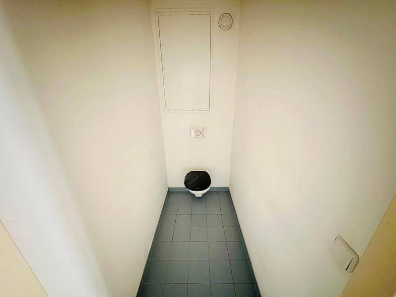 Separate Toilette mit Wand-WC und Fliesenboden in neutralen Farben.