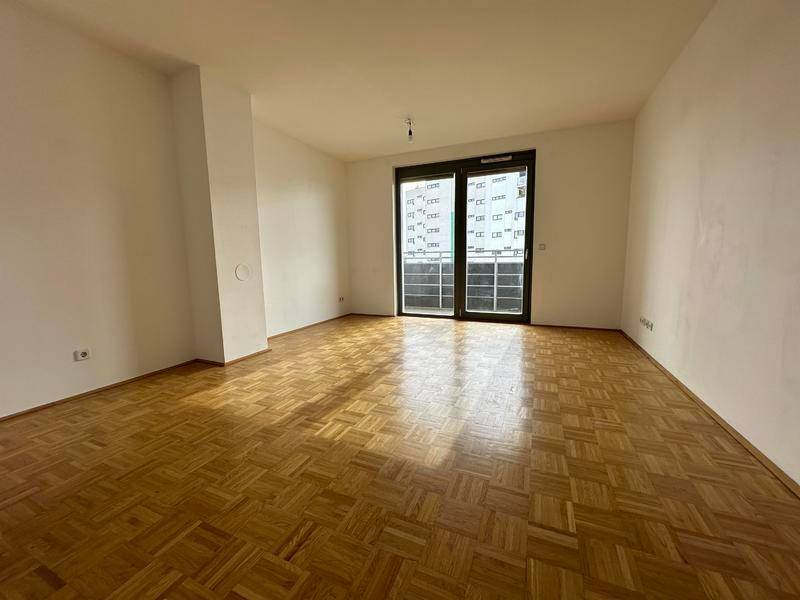 Heller Wohnbereich mit Parkettboden und großen Fenstern zum Balkon.
