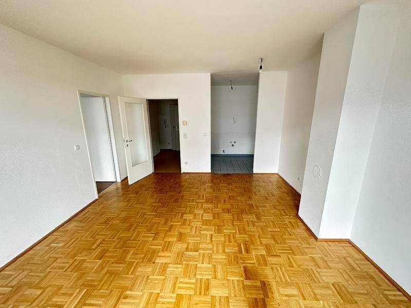 Wohnzimmer mit Parkettboden und offenem Zugang zum Küchenbereich.