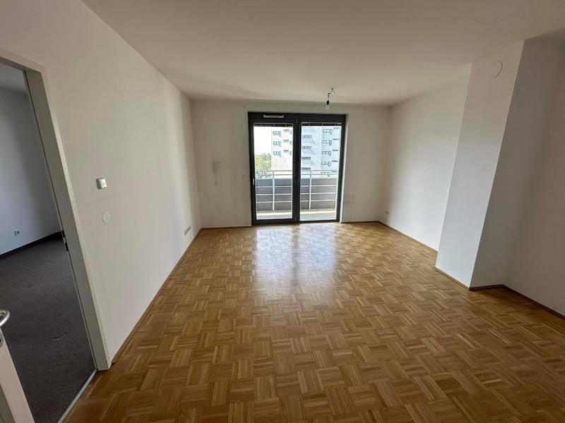 Heller, leerer Raum mit Fischgrätparkettboden und Zugang zu einem Balkon.
