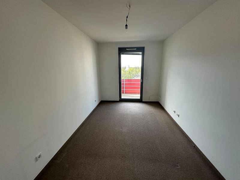 Leeres Schlafzimmer mit dunklem Teppichboden und Zugang zu einem Außenbereich.