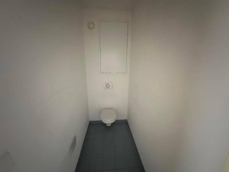 Separates WC mit wandhängender Toilette und grauen Bodenfliesen.