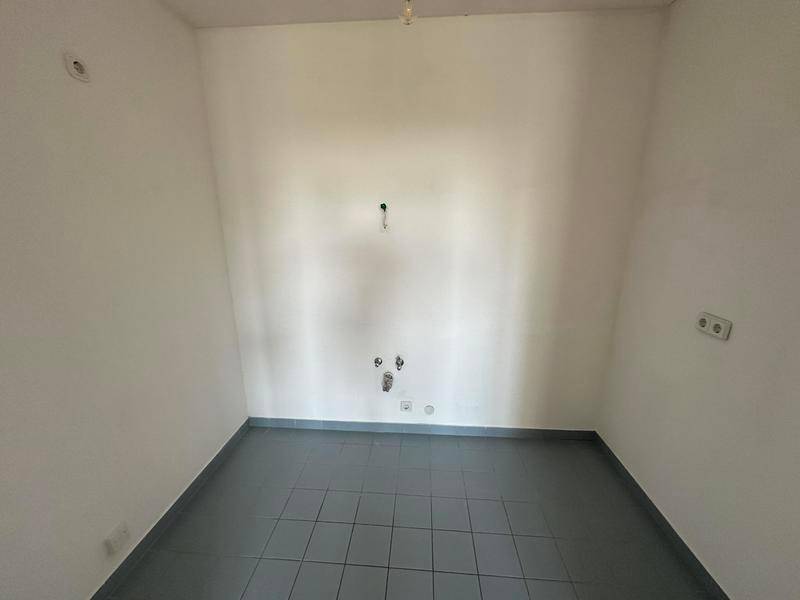 Leerer Küchenraum mit grauen Fliesen und Anschlüssen für Küchengeräte.