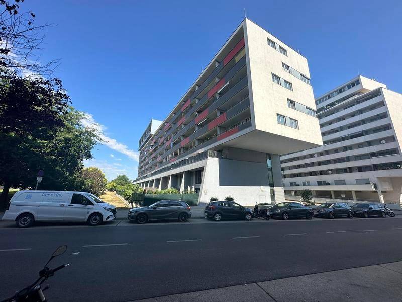 Modernes Wohngebäude mit auffälliger Architektur und geparkten Autos auf der Straße.