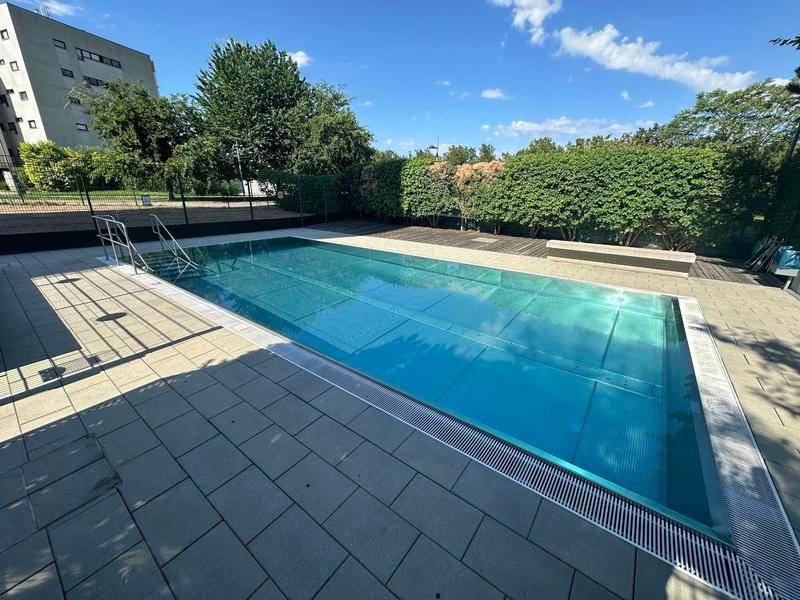 Großer Gemeinschaftspool mit gepflasterter Terrasse und umgebender Grünfläche.