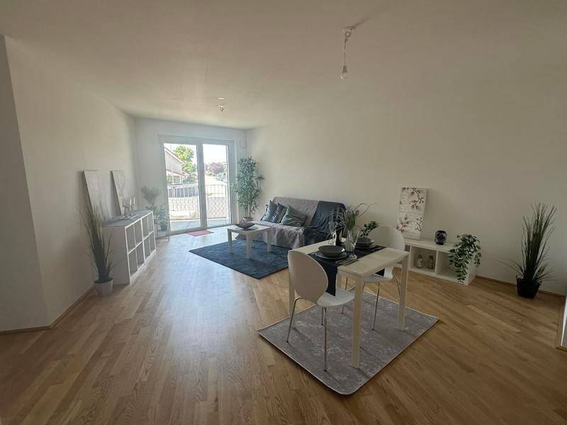 Heller offener Wohn-Essbereich mit Holzparkettboden und Zugang zum Balkon.