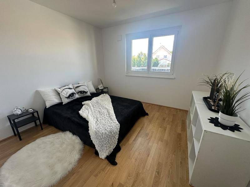 Schlafzimmer mit Holzboden, großem Fenster und minimalistischer Einrichtung in Schwarz-Weiß.