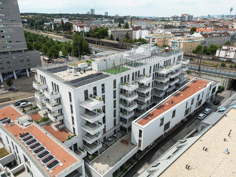 Luftaufnahme eines modernen Wohnkomplexes mit Dachterrassen, Solaranlagen und städtischer Umgebung.