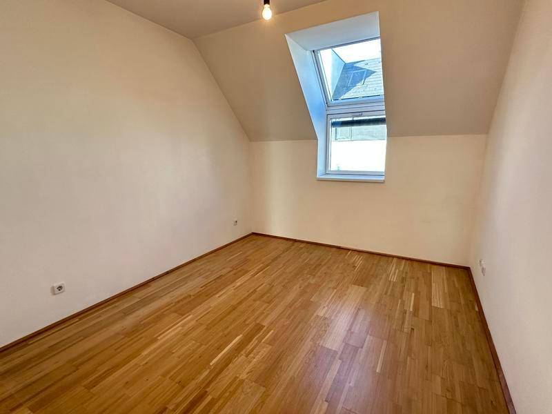 Leeres Schlafzimmer mit Holzparkettboden, Dachschräge und einem großen Dachfenster.