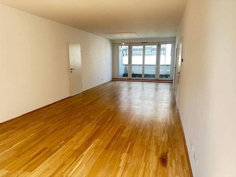 Geräumiges, leeres Wohnzimmer mit Holzparkettboden und Zugang zu einem Außenbereich.