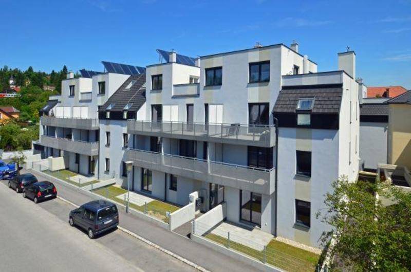 Ansicht eines modernen Wohngebäudes von der Straße aus, mit Balkonen und Parkplätzen.