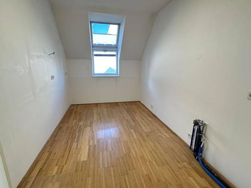 Leerer Raum mit Holzparkettboden und Anschlüssen für eine Küche, unter einem Dachfenster.