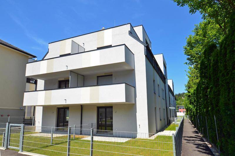 Moderne Fassade eines Neubaus mit Balkonen und gepflegten Grünflächen im Vordergrund.