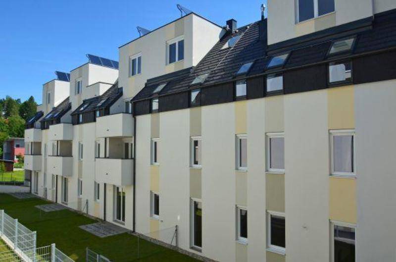 Seitenansicht eines modernen Wohngebäudes mit Balkonen, Dachfenstern und Photovoltaikanlagen.