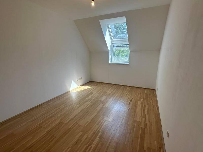 Helles Zimmer mit Holzparkettboden, Dachschräge und einem großen Dachfenster, ideal als Schlafzimmer.