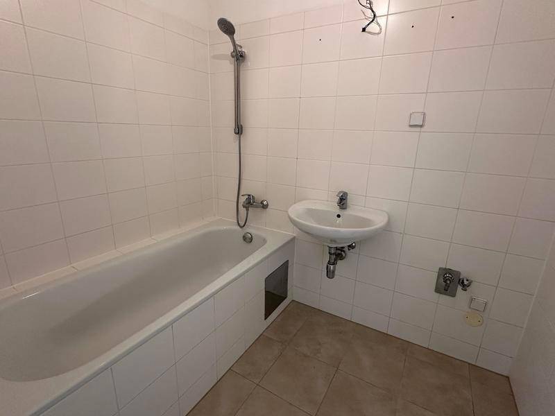 Badezimmer mit weiß gefliesten Wänden, Badewanne und einem einzelnen Waschbecken.