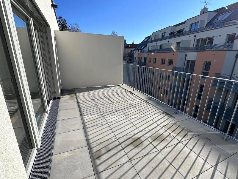 Geräumiger Balkon mit Fliesenboden und Metallgeländer, umgeben von modernen Gebäuden.