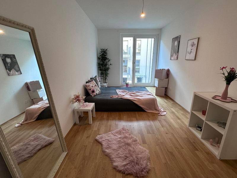 Schlafzimmer mit Holzboden, großem Spiegel und Zugang zum Balkon.