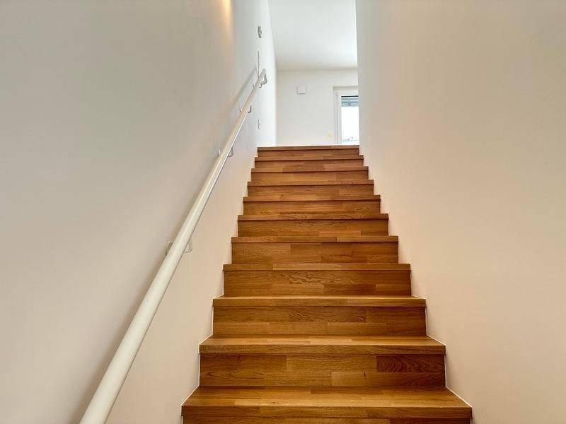 Helle Holztreppe mit weißem Handlauf, die die verschiedenen Wohnebenen miteinander verbindet.