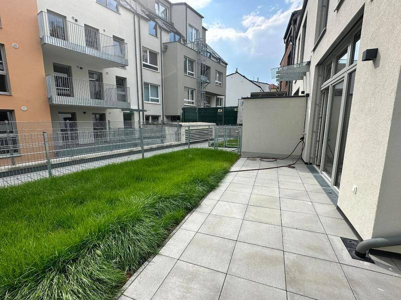 Gepflasterte Terrasse mit angrenzender Rasenfläche und Blick auf die moderne Wohnanlage.