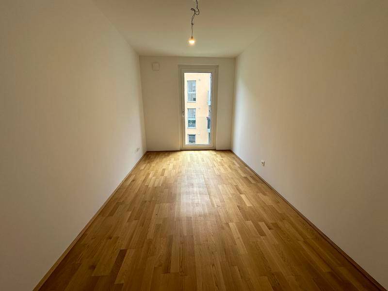 Heller Raum mit Holzboden und Fenster, geeignet als Schlafzimmer oder Arbeitszimmer.