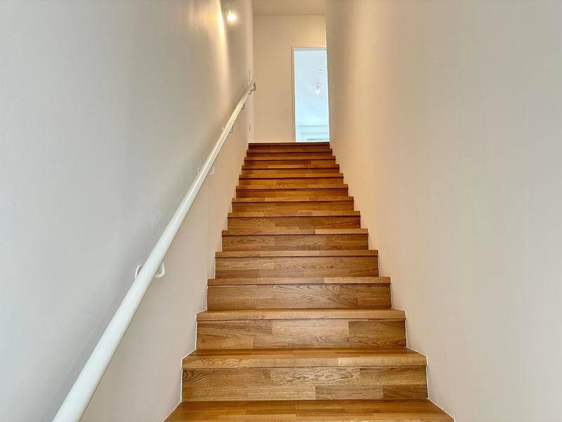 Moderne Holztreppe mit schlichtem Design und weißem Geländer, verbindet die Ebenen.