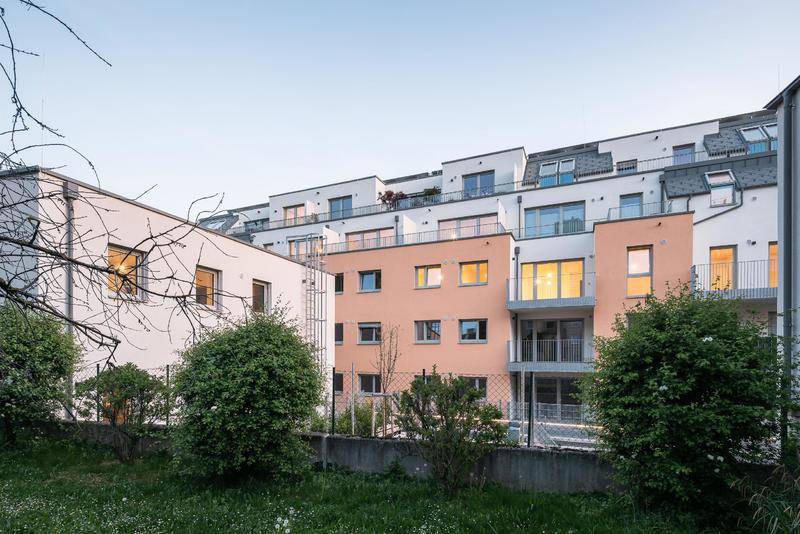 Moderne Wohnanlage bei Sonnenuntergang mit beleuchteten Balkonen und Grünflächen.