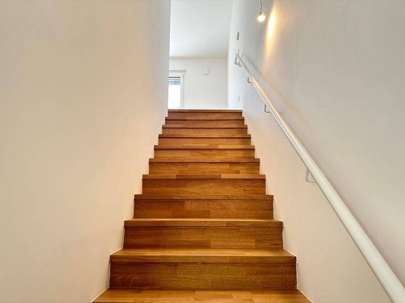 Heller Treppenaufgang mit Holzstufen und weißem Handlauf, der in die obere Etage führt.