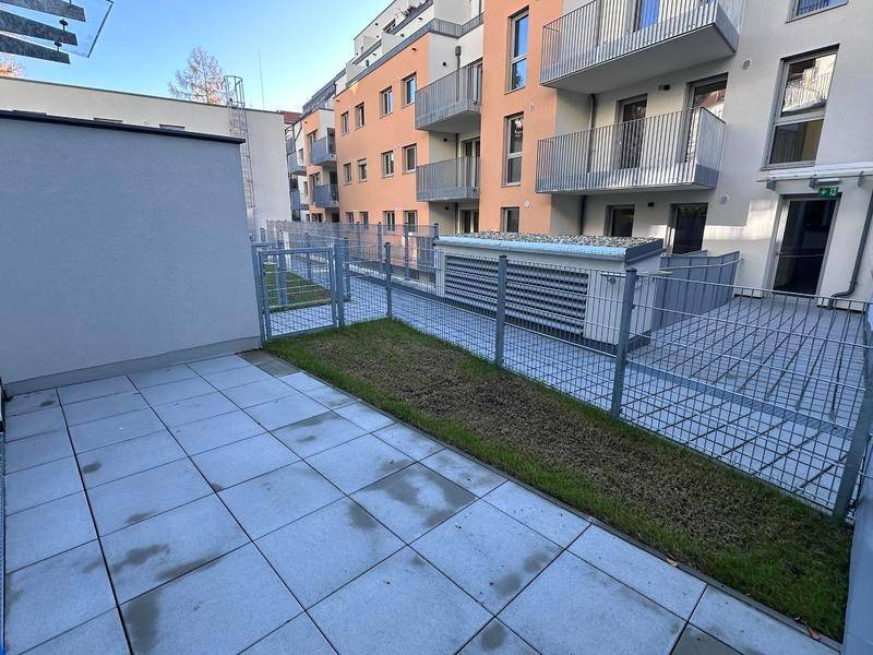 Gepflasterte Terrasse mit einem kleinen Rasenstreifen und Blick auf die Wohnanlage.