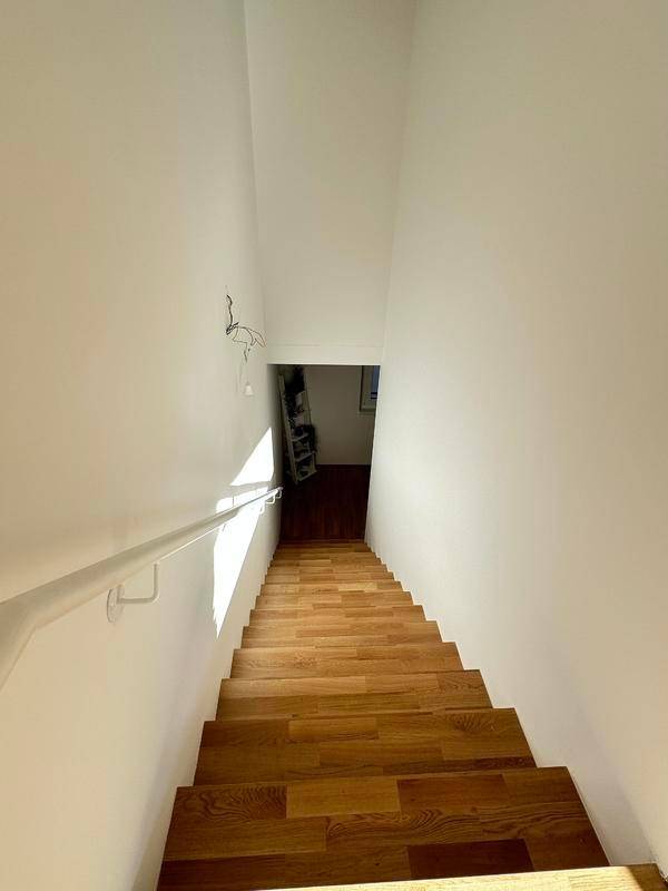 Heller Treppenaufgang mit Holzstufen und weißem Handlauf, der in die untere Etage führt.