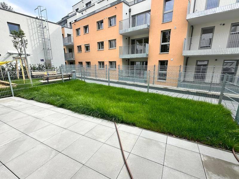 Kleiner privater Gartenbereich mit Rasenfläche und gepflasterter Terrasse vor einem Neubau.
