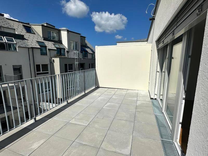 Geräumige Dachterrasse mit Fliesenboden und Metallgeländer, umgeben von Wohngebäuden.
