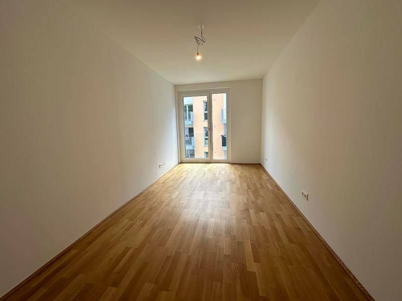 Helles Zimmer mit Parkettboden und großen Fenstern, die viel Tageslicht hereinlassen.