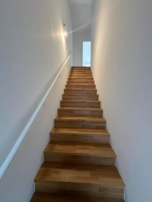 Heller Treppenaufgang mit Holzstufen und weißem Handlauf, der zu den oberen Etagen führt.