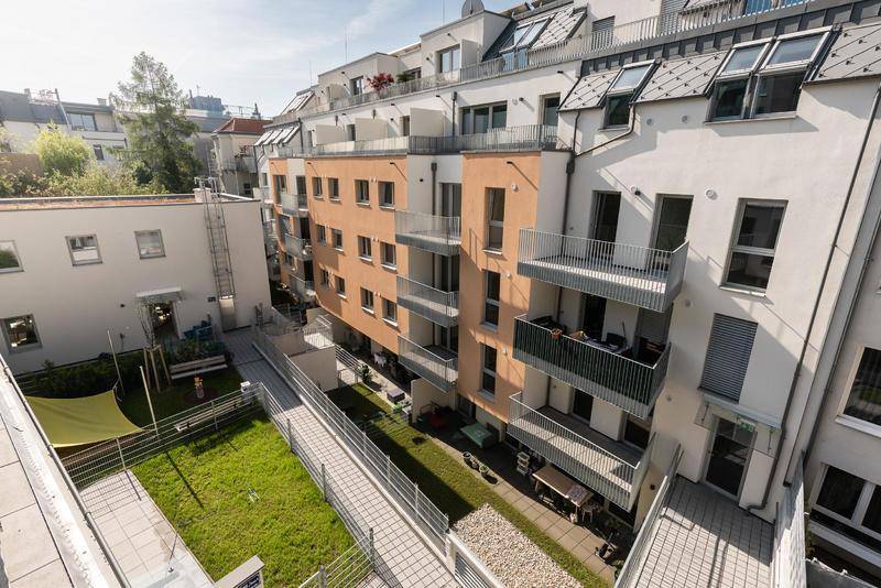 Luftaufnahme eines modernen Wohnkomplexes mit begrüntem Innenhof, Spielplatz und Balkonen.