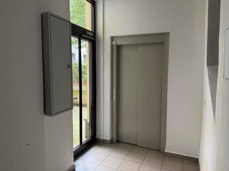 Eingangsbereich mit Aufzug und großer Glastür, die nach draußen führt.