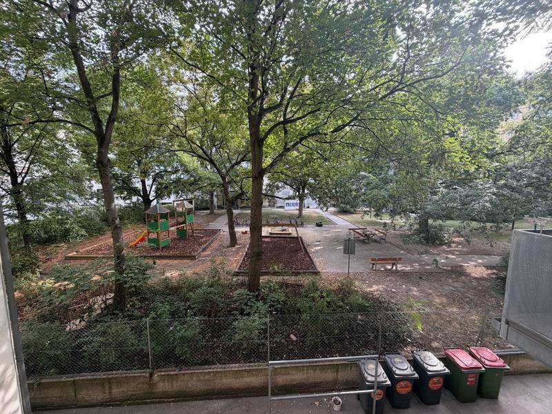 Blick auf einen grünen Innenhof mit Spielplatz und vielen Bäumen.