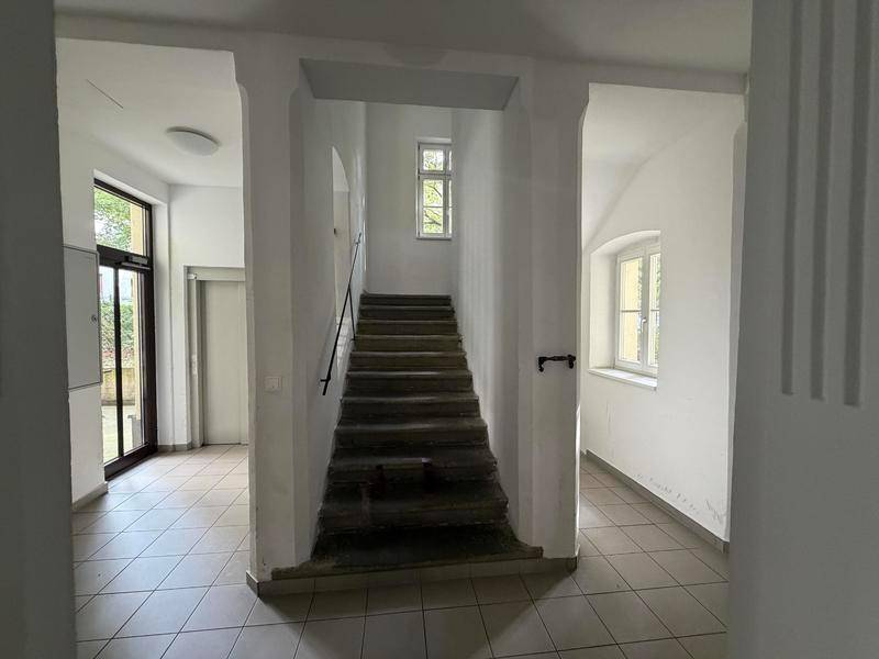 Treppenhaus in einem Mehrfamilienhaus mit Fliesenboden und Fenstern für Tageslicht.