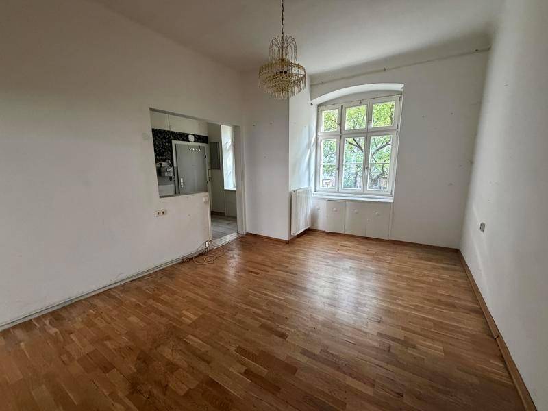Helles Wohnzimmer mit klassischem Parkettboden, großem Fenster und Kronleuchter.